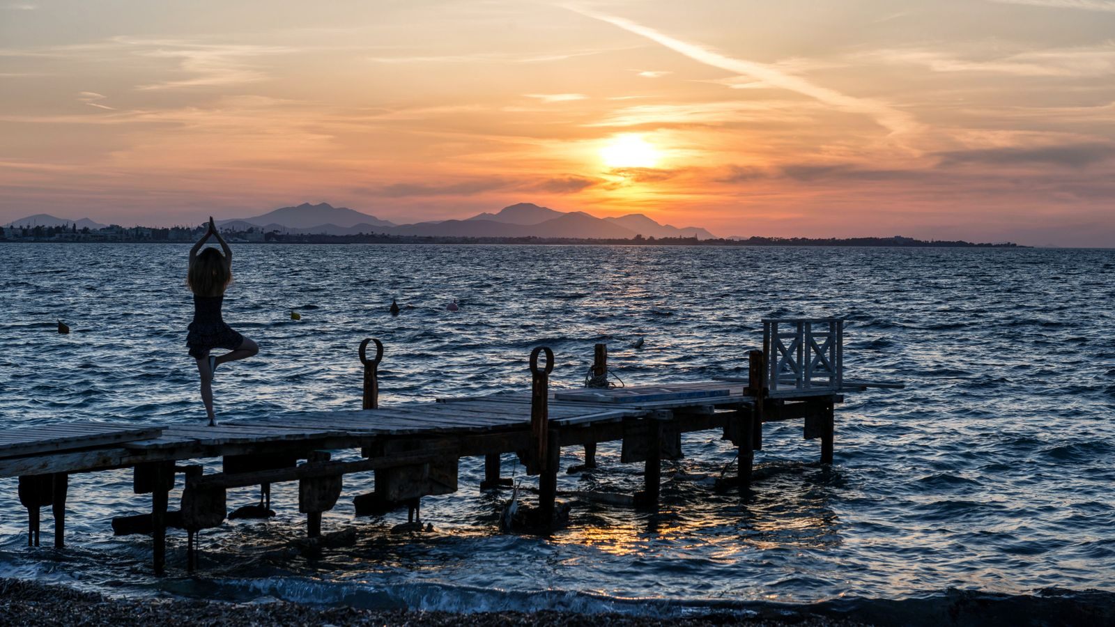 Niche cruises for every passion: a woman holding a yoga pose on a jetty above the sea at sunset